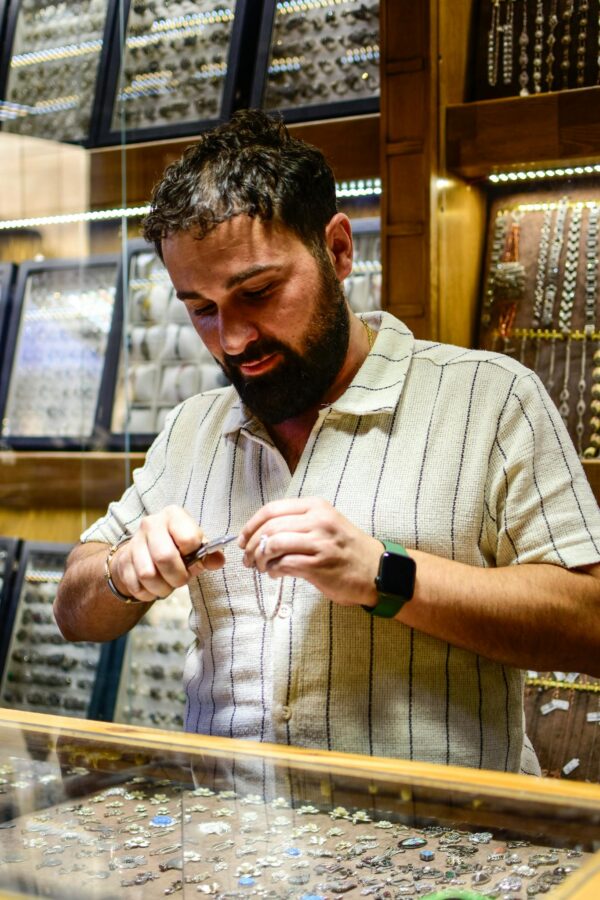 A bearded jeweller inspects jewelry in a shop, showcasing his craft and expertise.