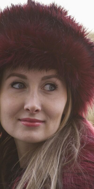 Stylish woman wearing a red fur hat, captured in a candid outdoor portrait.